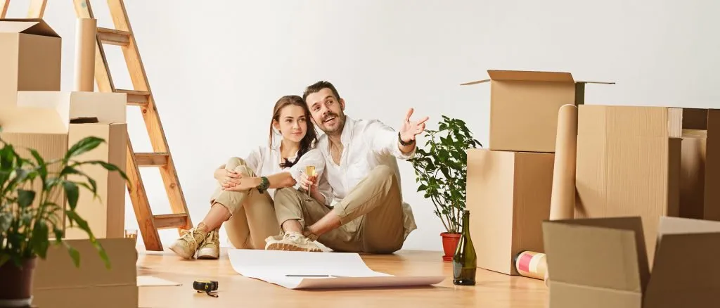A couple sitting on the floor among packed cartons pointing out plans for their new home
