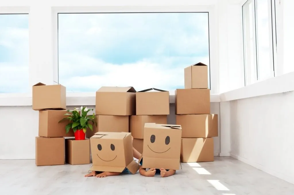quickandeasy_slide_one Two children hiding behind cardboard boxes drawn with smiley faces in a bright empty room