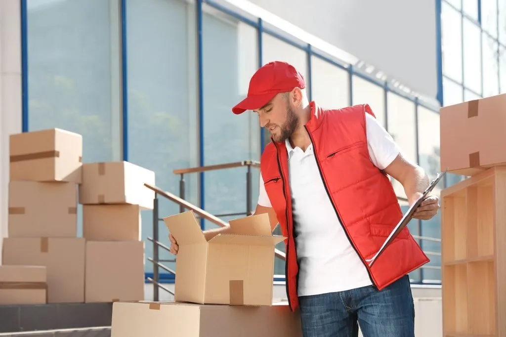 removalists-planning A mover in a red vest checking an inventory clipboard beside stacked moving boxes